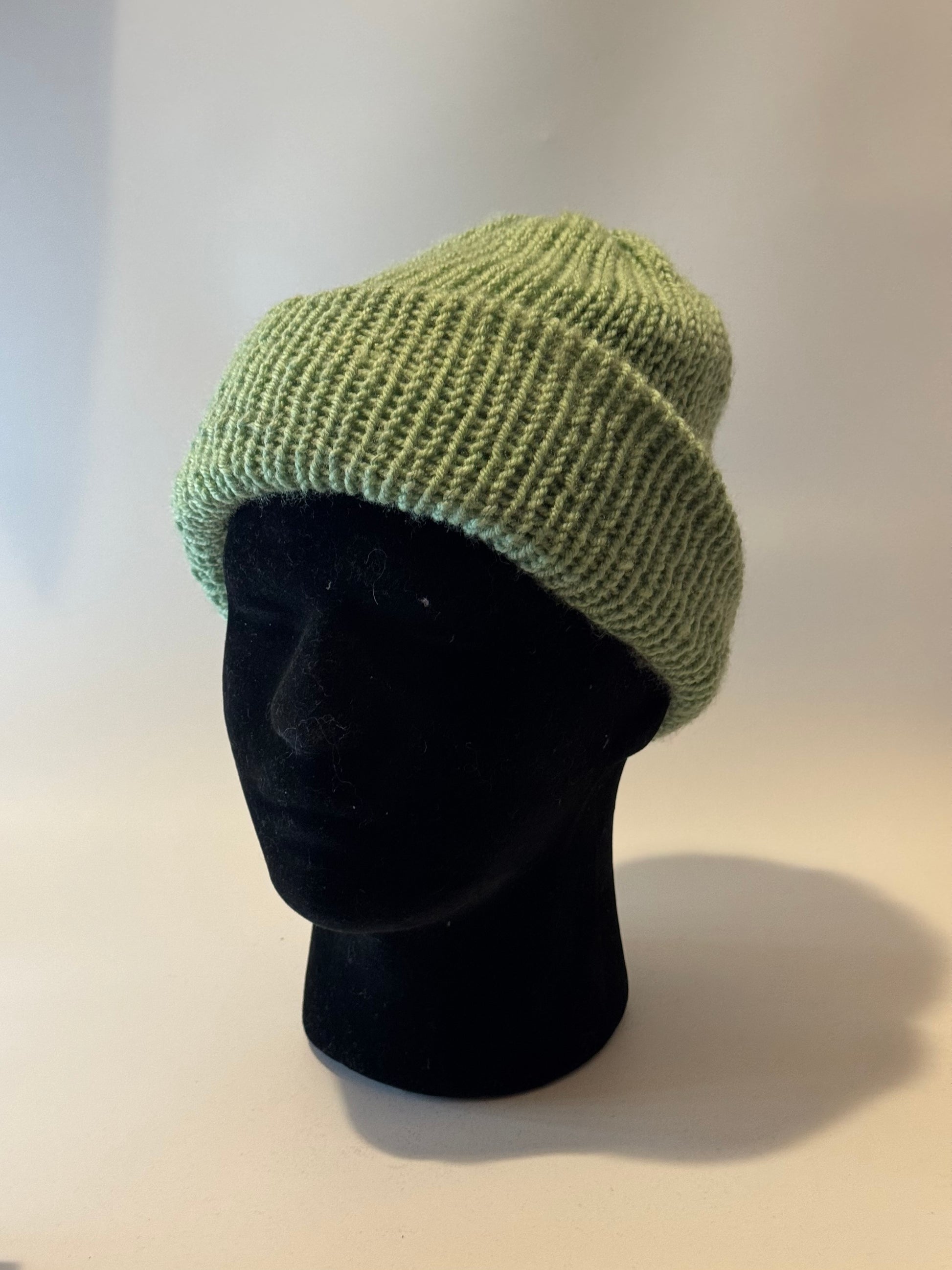 Green knit beanie on a black mannequin head against a white background