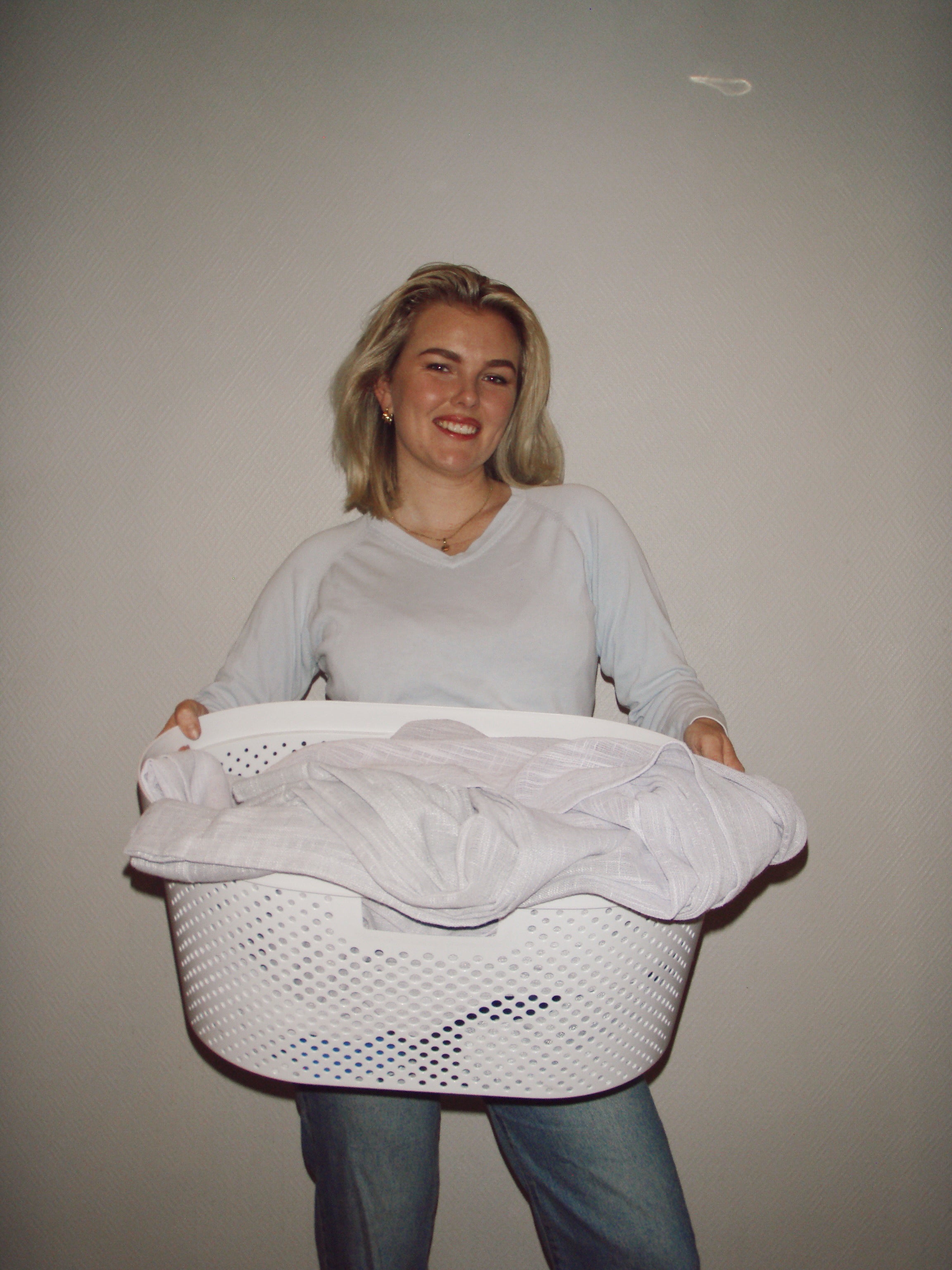 Person holding a white laundry basket with clothes against a plain background