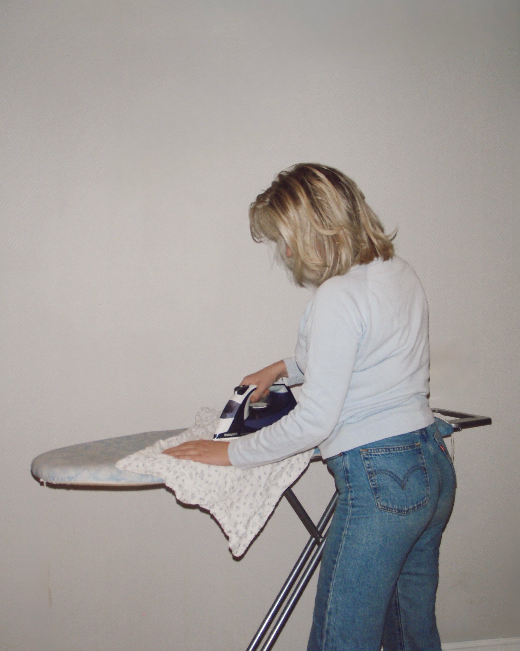 Person ironing a shirt on an ironing board against a plain wall.